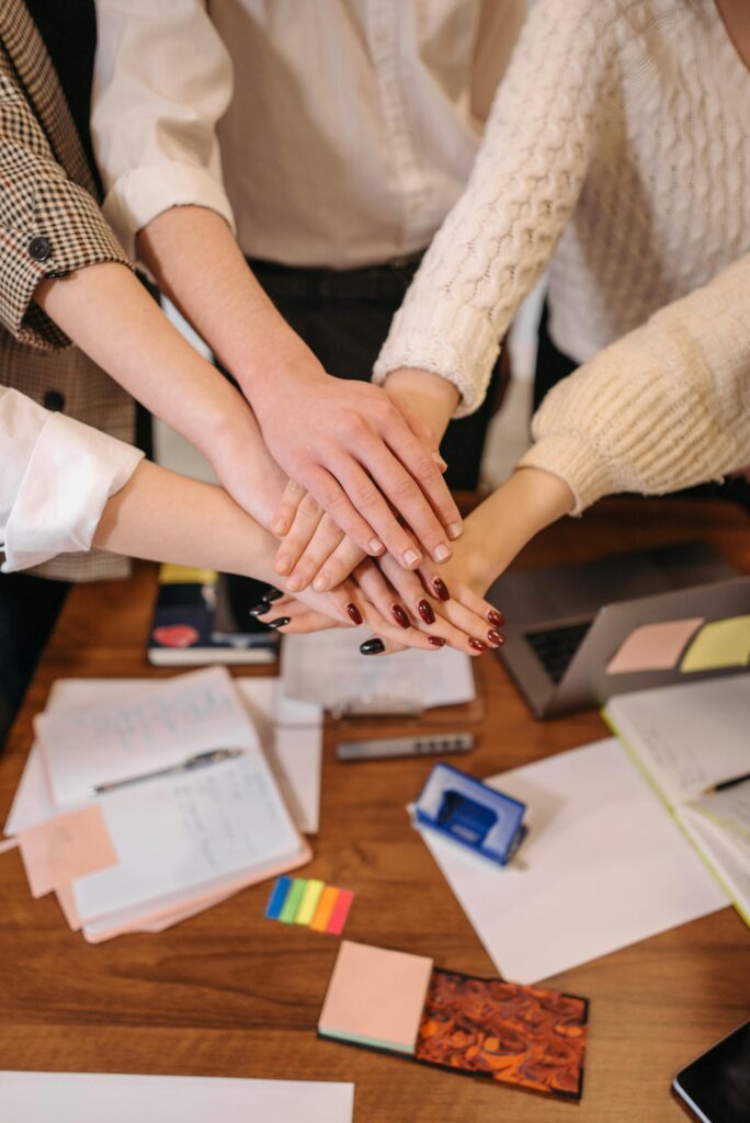 A top-down view of hands stacked together over an office table, symbolizing teamwork.